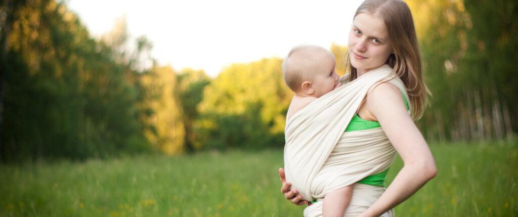 mother carrying daughter in sling in field